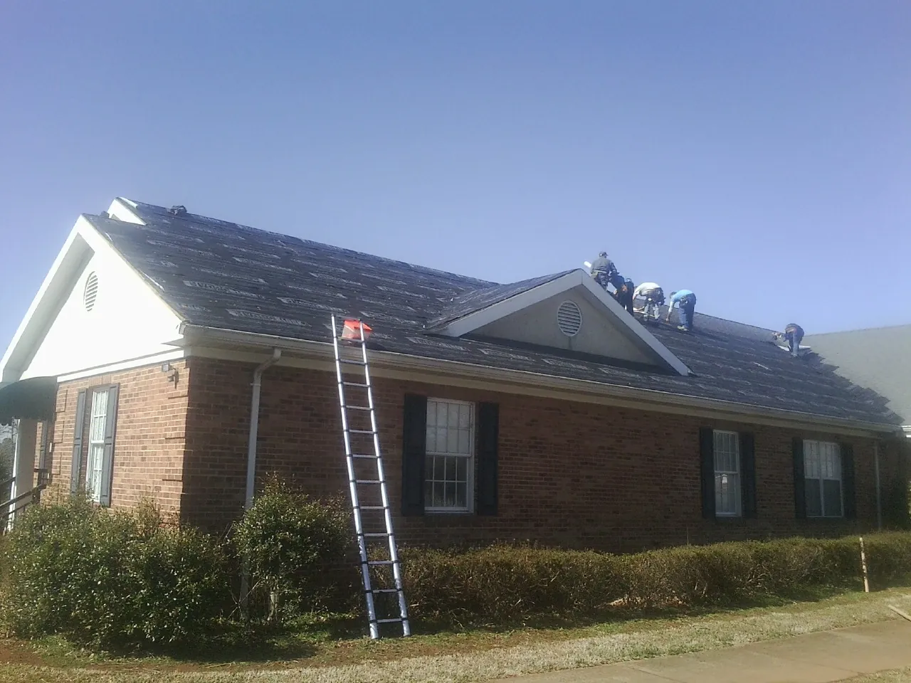 Crew tearing shingles off a brick ranch roof with a ladder set — Metal Roof Repair work by our crew in Finksburg