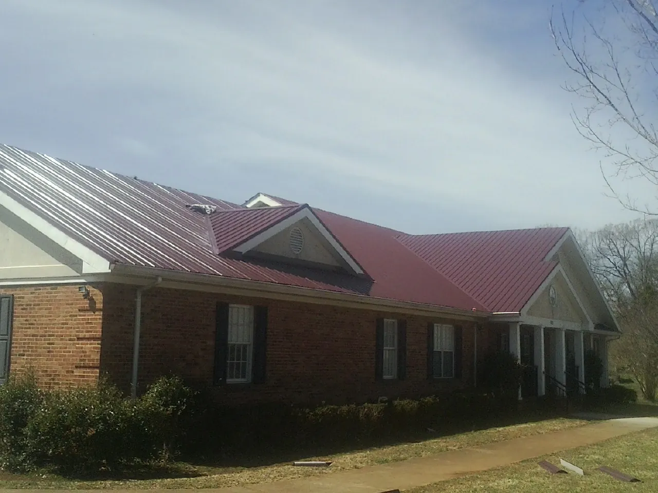 Red metal roof with gabled entries on a long brick building, from a Hail Damage Roof Repair job in Finksburg