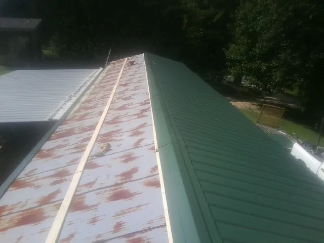 Old rusted panels beside newly installed green metal roofing — Wind Damage Roof Repair by Roofing Brothers in Finksburg