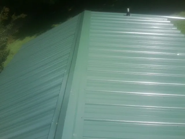 New green metal panels meeting at the ridge of a roof — Flat Roof Repair work by our crew in Finksburg