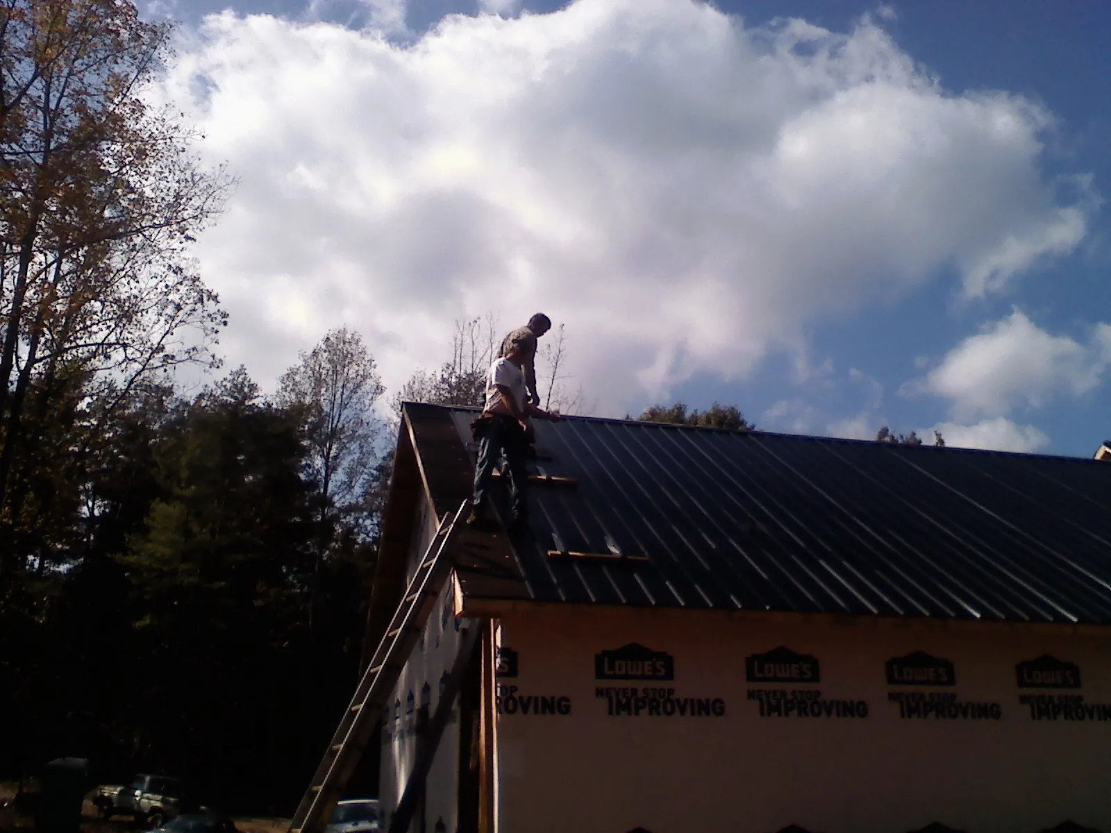 Roofer fastening dark metal panels high against a cloudy sky, from a Roof Inspection job in Finksburg